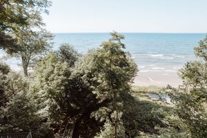Scenic coastal view through trees showing turquoise waters and sandy beach below.