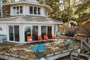 Charming waterfront cottage with orange deck chairs and turquoise accents features a wraparound deck and bay windows.