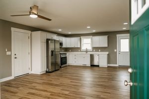 Modern open concept kitchen with white cabinets, stainless appliances and hardwood floors in renovated space with turquoise door.