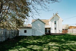 Small white church building with tall spires and green lawn surrounded by a metal fence on a sunny day.