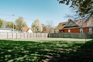 A grassy backyard enclosed by wooden privacy fences with brick houses and trees visible in the background.