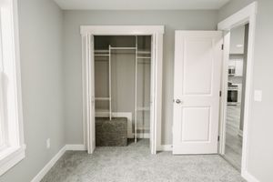 An empty bedroom with gray carpet, white walls, and two closets with open doors revealing built-in storage spaces.