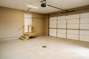 Spacious unfinished garage interior with beige walls, concrete floor and wooden workbench.