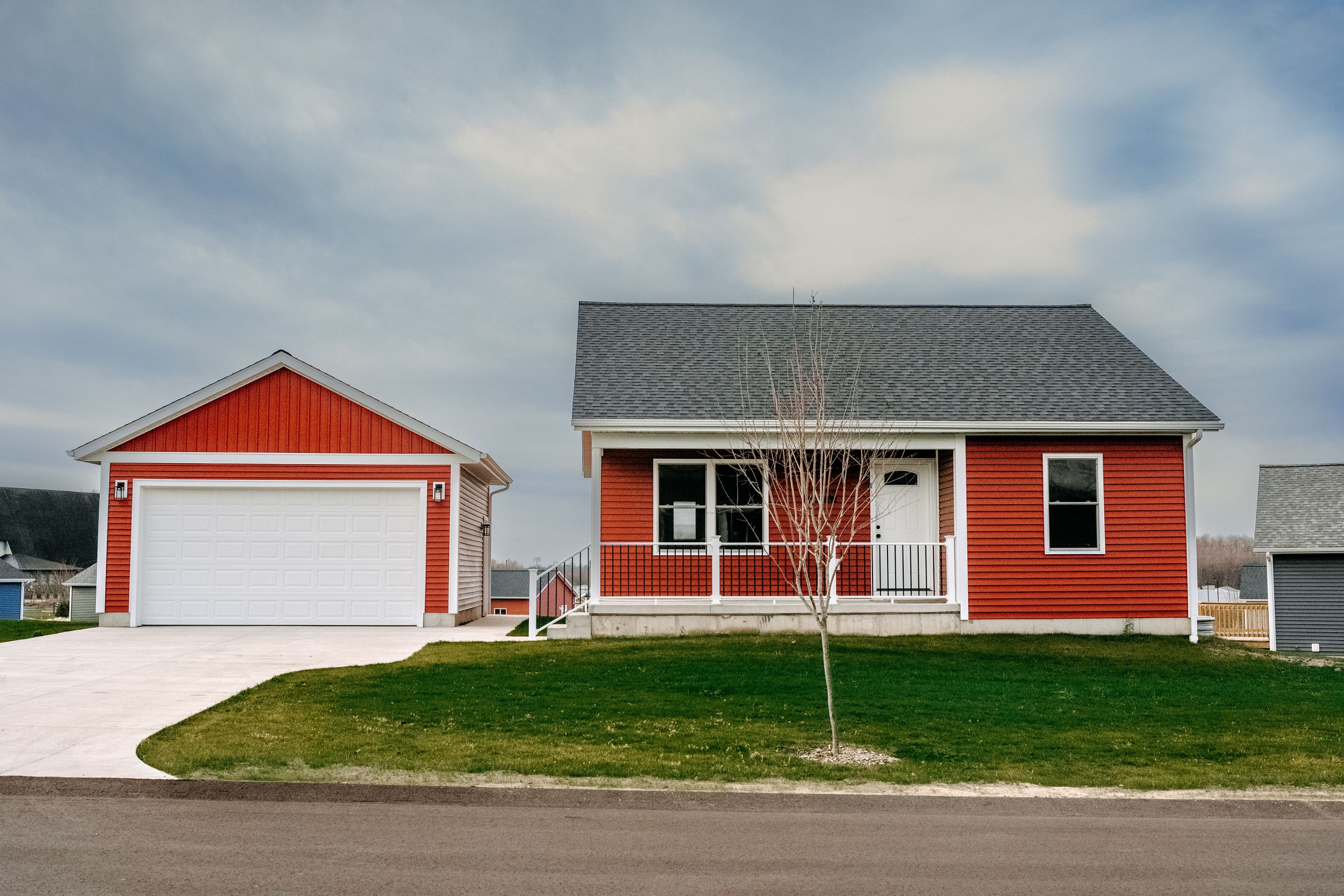 Modern red ranch-style house with attached garage and neatly maintained lawn on a gently sloped lot.