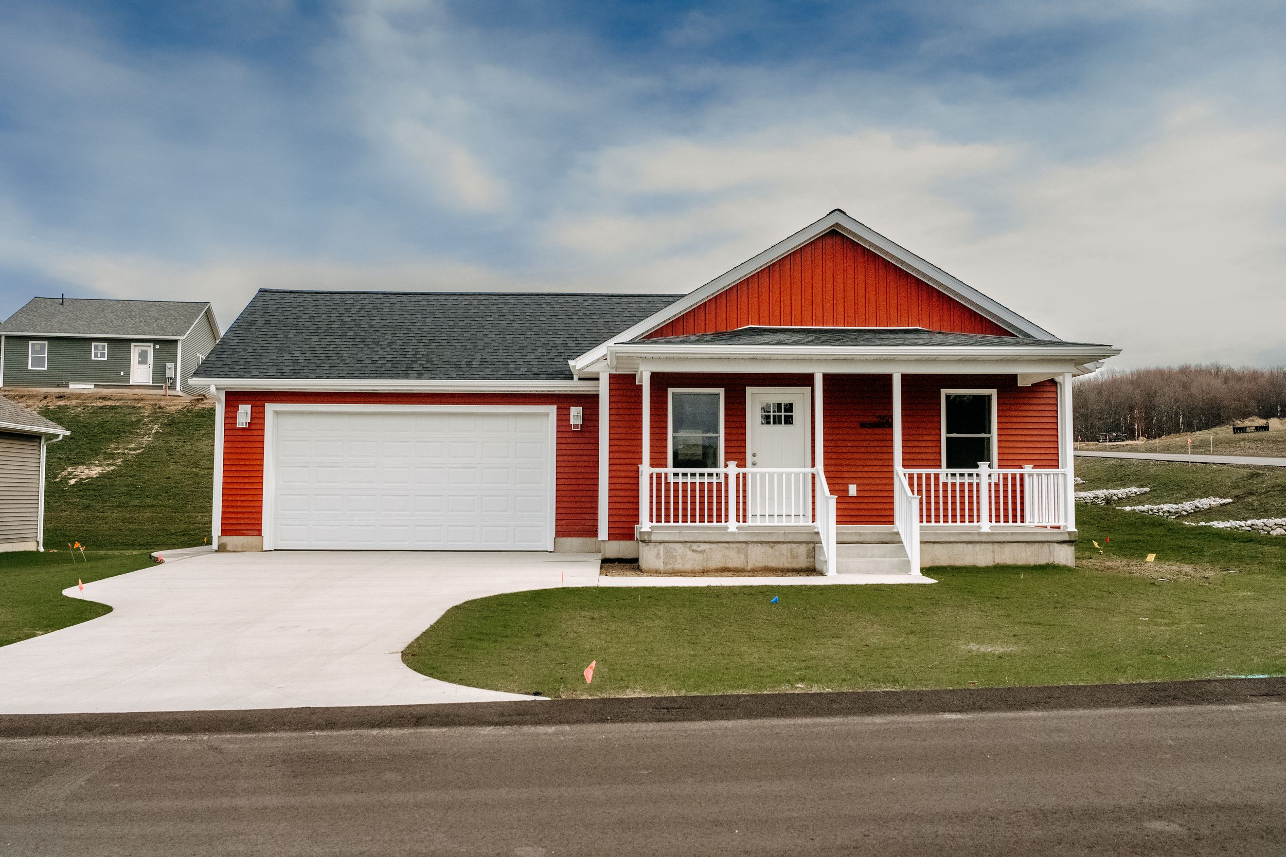 A charming red ranch house with white trim features a covered front porch and attached two-car garage on a grassy lot.