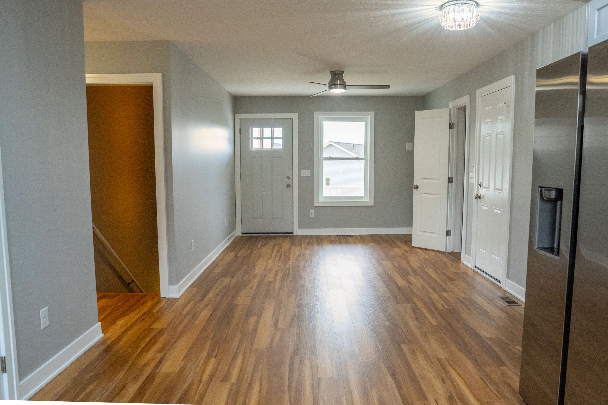 Modern interior hallway with hardwood flooring, gray walls, and white doors illuminated by ceiling lighting.