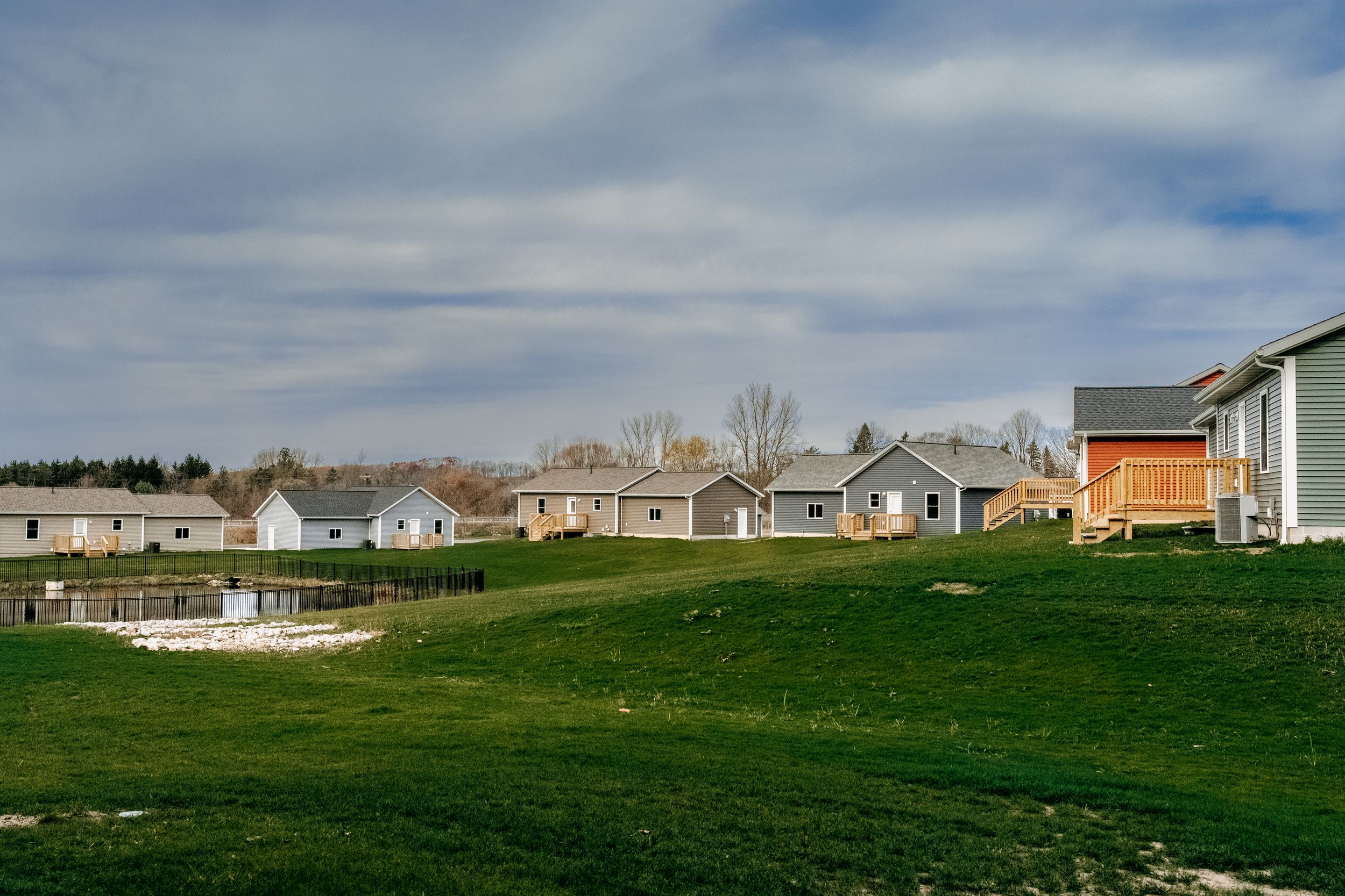 Row of suburban houses along green lawn on a cloudy day in residential neighborhood development.