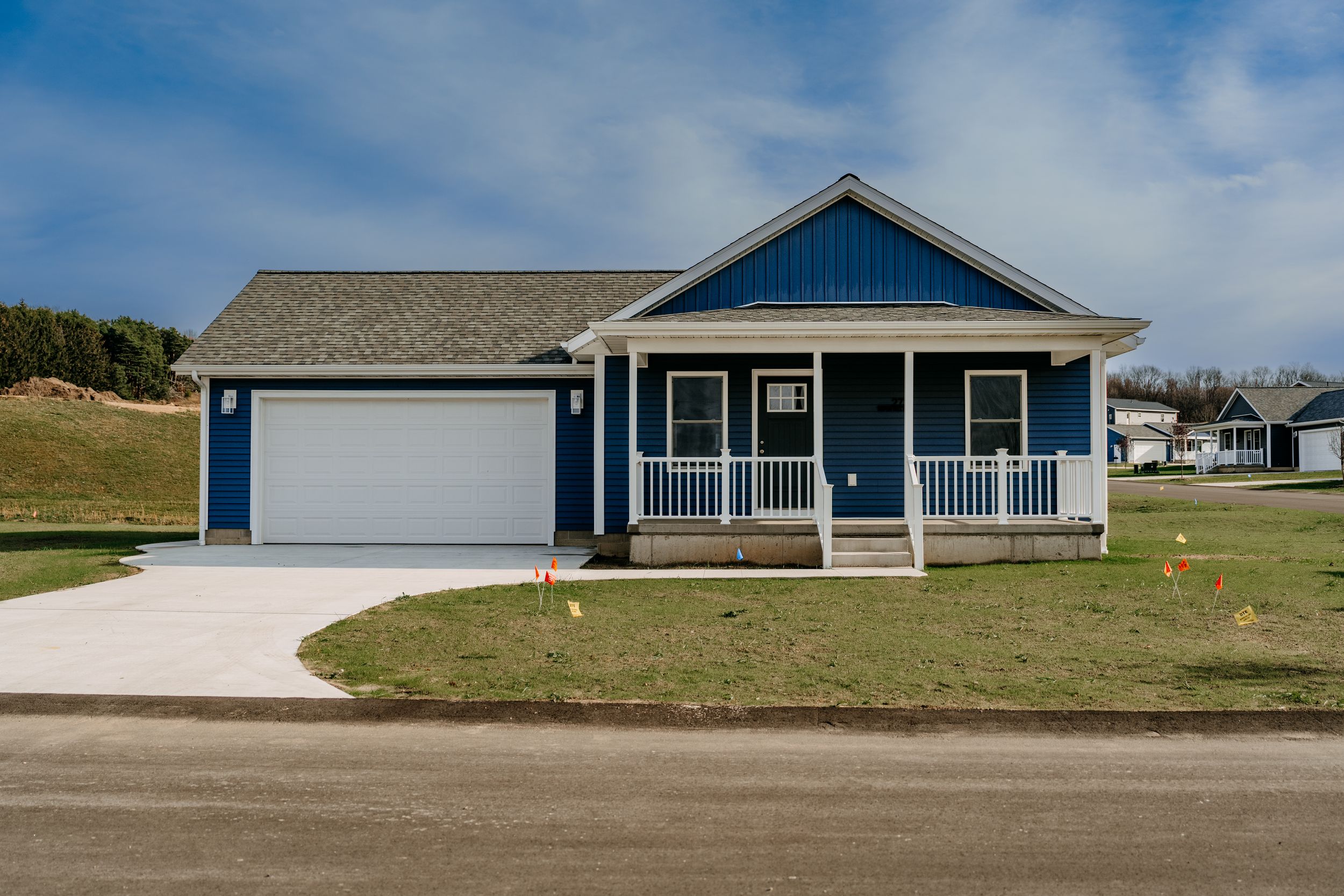 Blue single-story ranch home with covered front porch, gray trim, and attached garage on a sloped lawn.