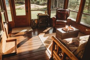 Cozy train car interior with sunlit wooden floors, brown leather chair, and vintage trunks by panoramic windows.