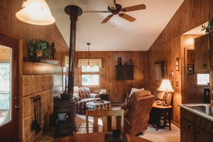 Cozy rustic cabin interior with wood paneling, wood stove, leather furniture, and warm lighting creating an inviting atmosphere.