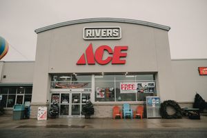 Exterior view of Rivers Ace Hardware store entrance with red logo signage on gray building facade.