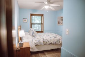 A cozy bedroom with light blue walls, wooden trim, a ceiling fan, and floral bedding on a queen-sized bed.