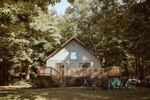 A charming A-frame cabin with a wooden deck and blue Adirondack chairs nestled in a peaceful forest setting.