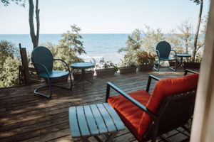 Red cushioned patio furniture on a wooden deck overlooking a peaceful lake view through trees on a sunny day.