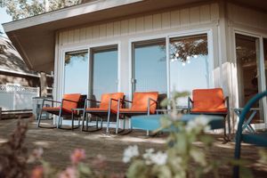 Modern beach house deck with orange chairs and blue cushions facing the ocean.