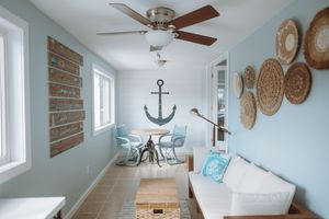 Coastal-themed narrow room with turquoise walls, anchor decor, woven baskets, white couch and ceiling fan in beach house style.