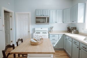 Modern kitchen interior with light blue cabinets, wood dining table, and white appliances in an L-shaped layout.