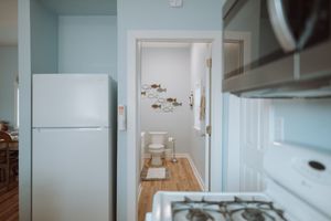 Small apartment kitchen interior with white refrigerator and view into bathroom with wooden flooring.