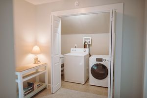 A clean laundry room with white appliances and a small table lamp beside the doorway.