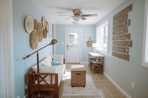 A bright coastal entryway features light blue walls, woven basket wall decor, and natural wood furniture.
