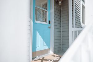 Light blue front door with white trim against gray siding creates a welcoming coastal entrance.