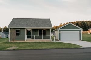 Small single-story ranch home with gray vinyl siding and matching detached garage on a grassy lot.