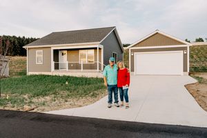 New modern beige house with front porch and detached garage connected by concrete driveway on hillside property.