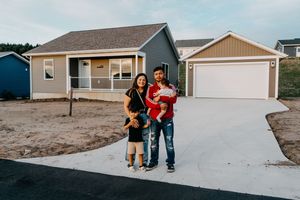 Family stands in front of a new single-story home with detached garage and freshly poured concrete driveway.