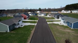 Aerial view of small houses arranged along a paved road in a residential development with green lawns.
