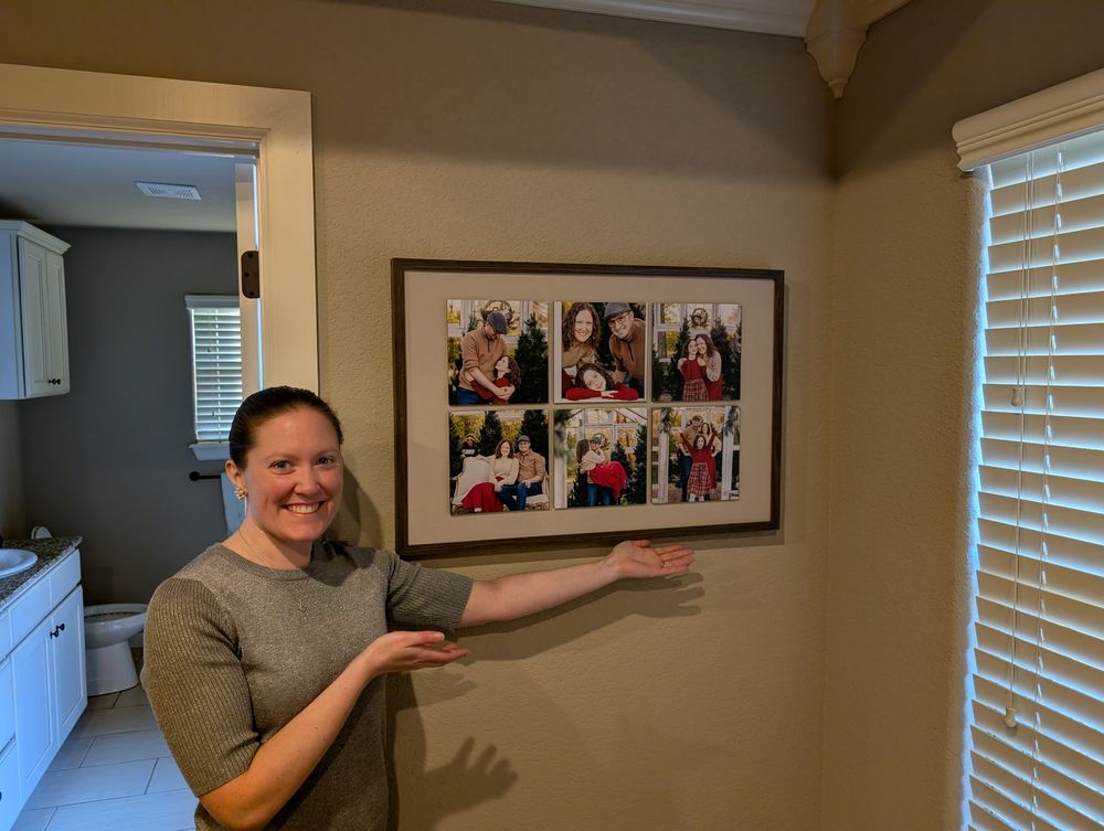 Person gesturing dramatically while standing in a room with framed photos on the wall and window blinds.