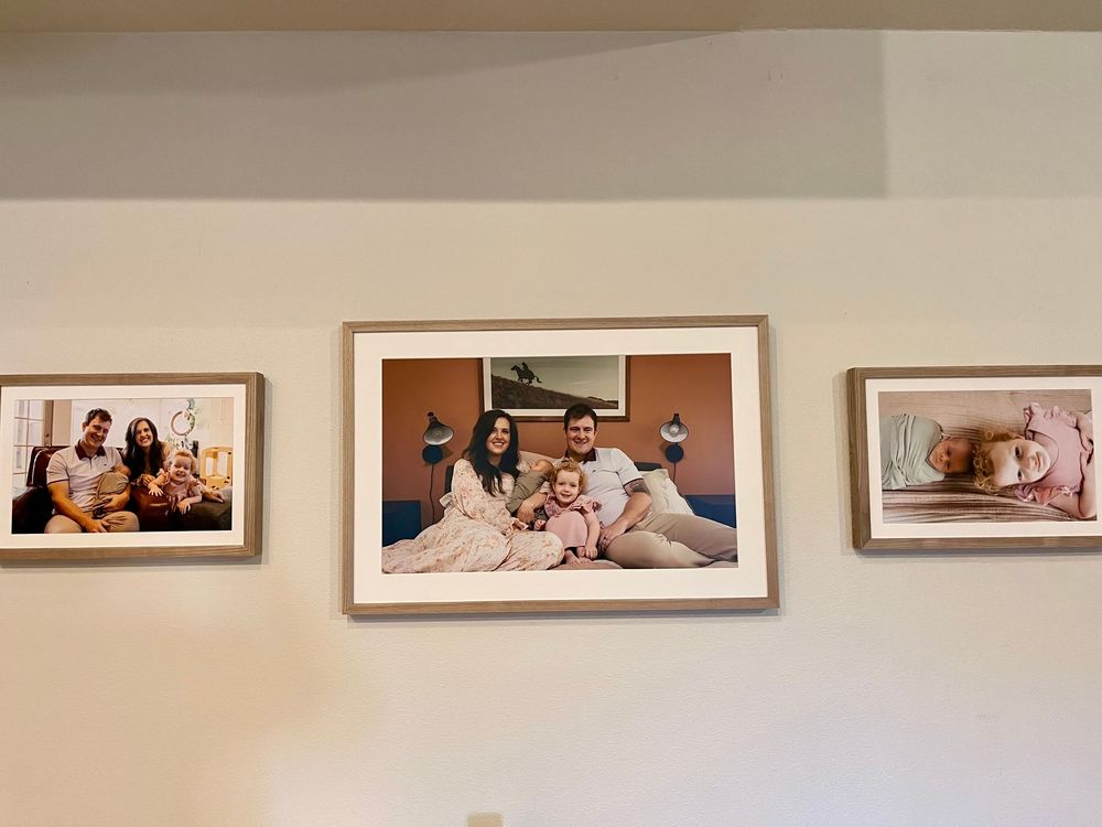A gallery wall displays multiple framed photographs in a horizontal line against a beige painted wall.
