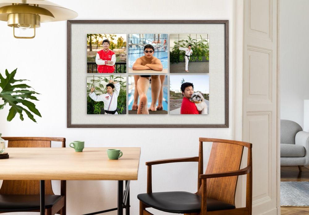Gallery wall arrangement featuring framed artwork and photos above a wooden dining table with chairs in a bright room.