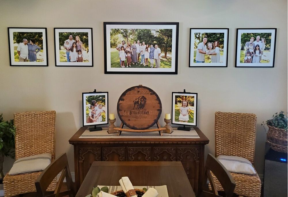 A rustic wooden table displays family photos on the wall above it, with wicker chairs and a decorative barrel accent.