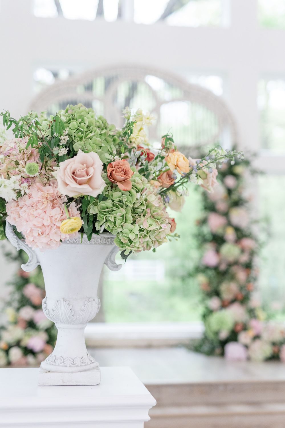 White urn vase with romantic garden-style arrangement of blush roses, hydrangeas, and greenery.