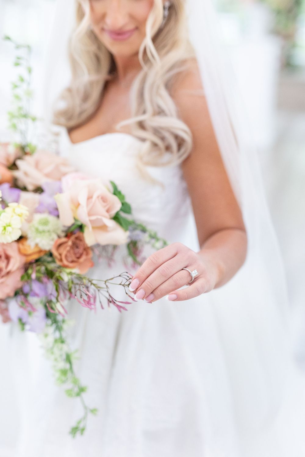 Bride holding a pastel wedding bouquet with peach roses, showing her diamond engagement ring and manicured nails.