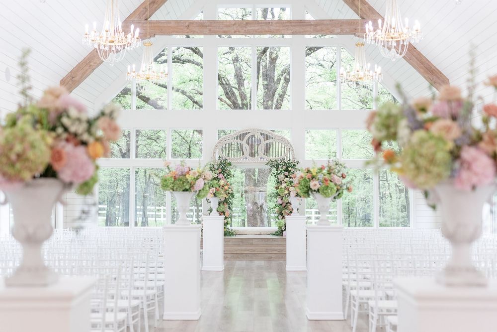Bright white wedding chapel interior with chandeliers, floral arch, and white chairs lining the aisle.