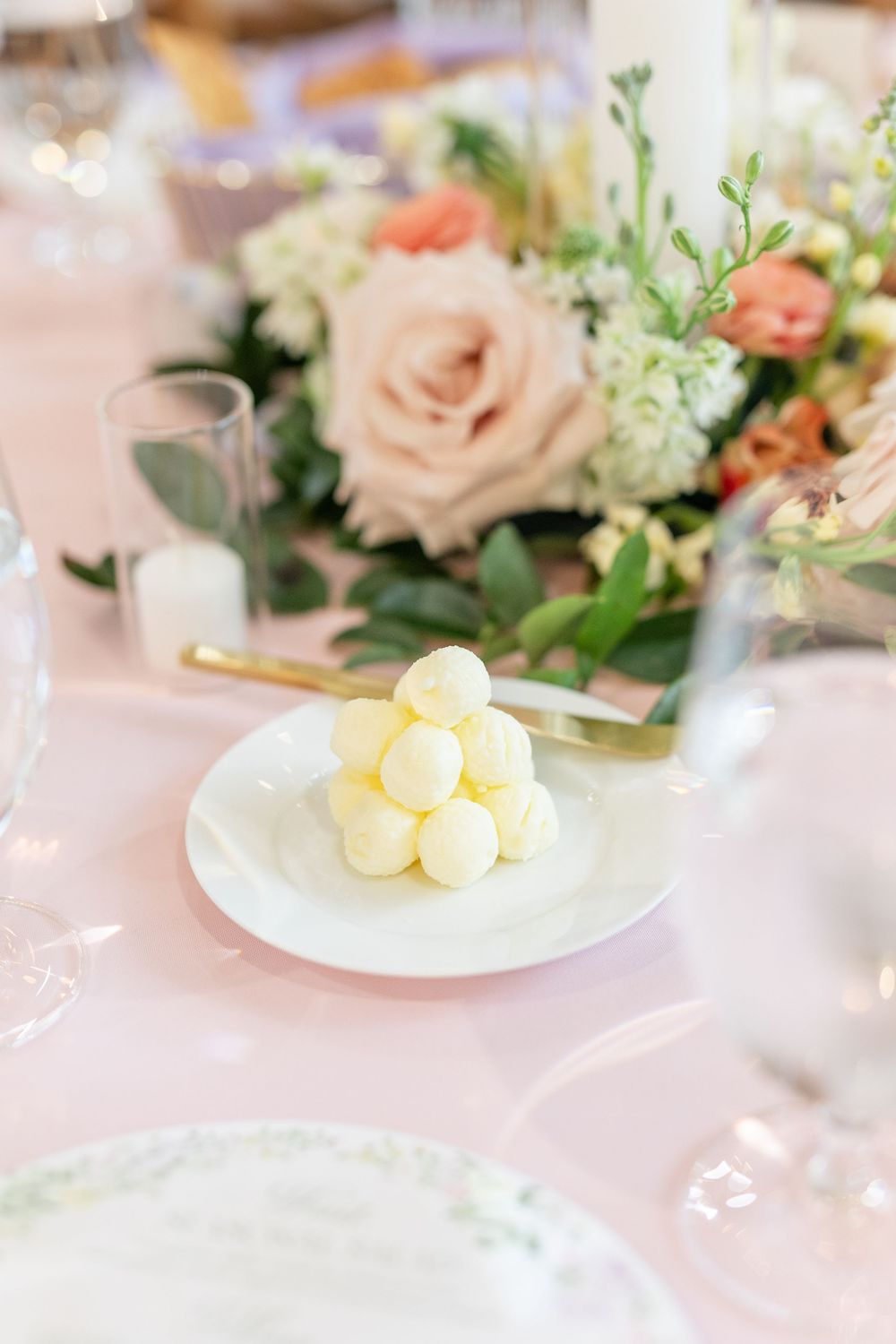 White chocolate truffle pyramid on a plate beside blush floral centerpiece at a wedding reception.