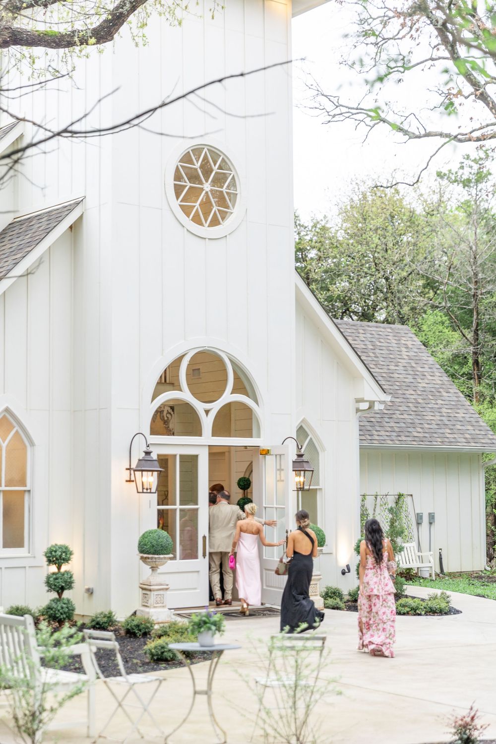 Guests arriving at a charming white chapel wedding venue with arched windows and lantern sconces.