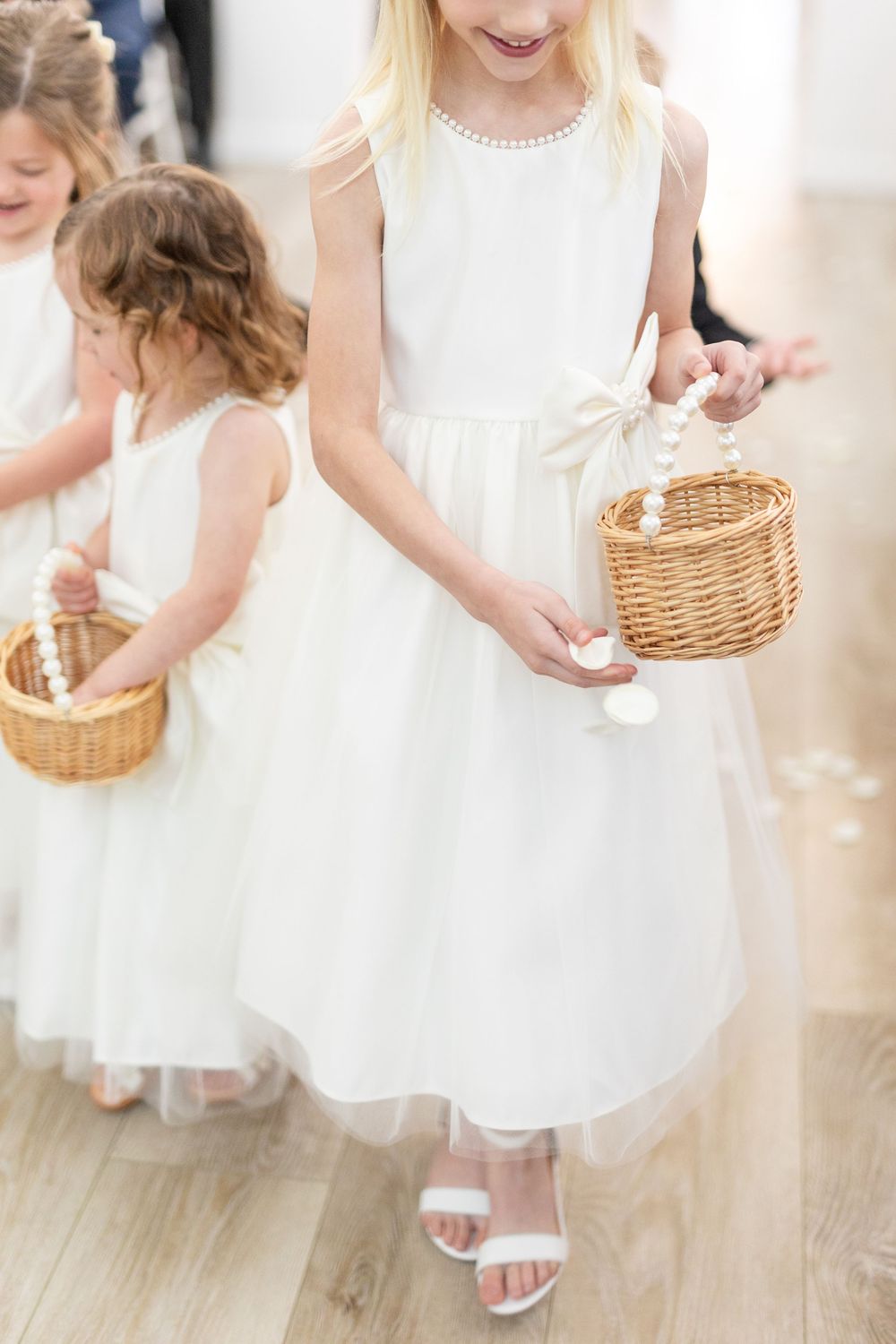 Adorable flower girls in white dresses scattering petals from wicker baskets down the wedding aisle.
