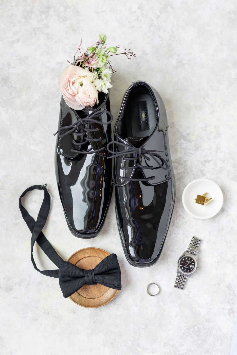Black patent leather groom shoes with bow tie, watch, and cufflinks wedding detail flatlay.