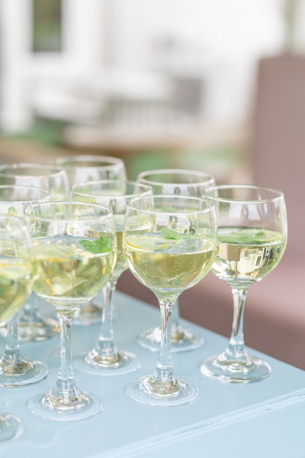Row of wine glasses filled with white wine and fresh mint garnish on a light blue tray.
