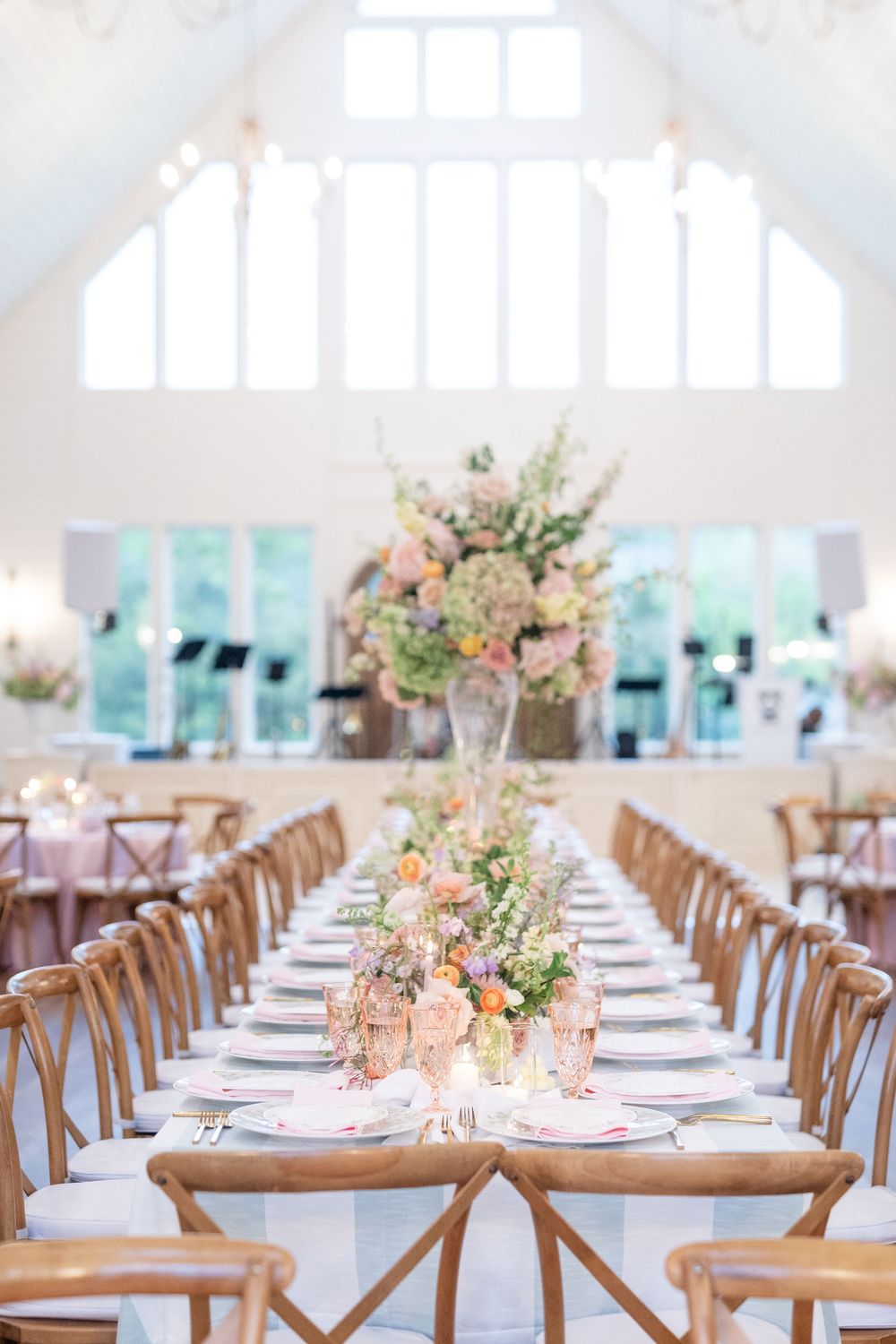 Long reception table with tall floral centerpieces in pastel pink and white blooms in bright white venue.