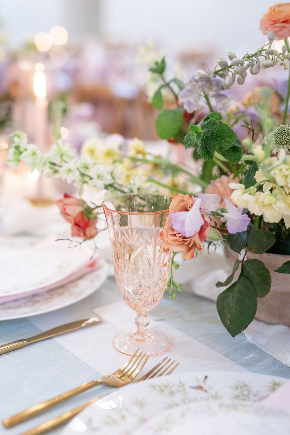 Close-up of wedding place setting with pink crystal goblet, gold flatware, and colorful floral centerpiece.