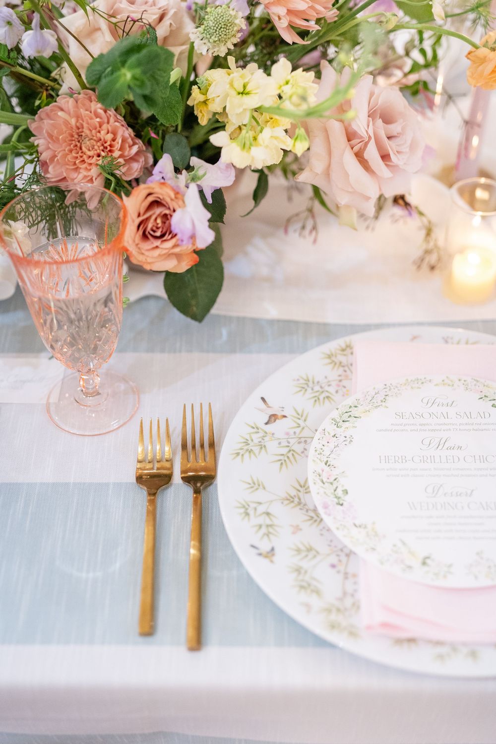 Elegant wedding place setting with gold flatware, pink goblet, floral china, and printed menu card.
