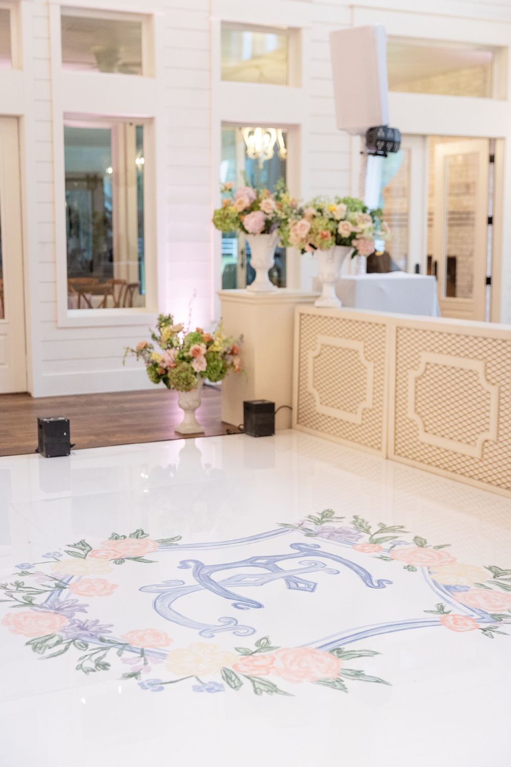 White wedding dance floor featuring a painted floral monogram wreath with pastel roses and blue initials.