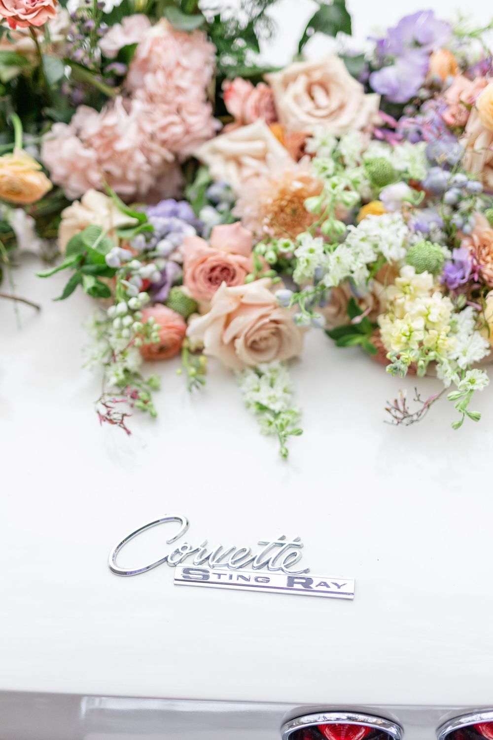 Elegant Corvette Stingray emblem surrounded by lush pastel pink, peach, and lavender floral wedding decorations.