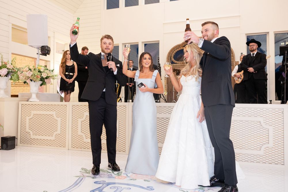 Wedding party celebrates with champagne bottles raised on a decorated dance floor during a lively reception.