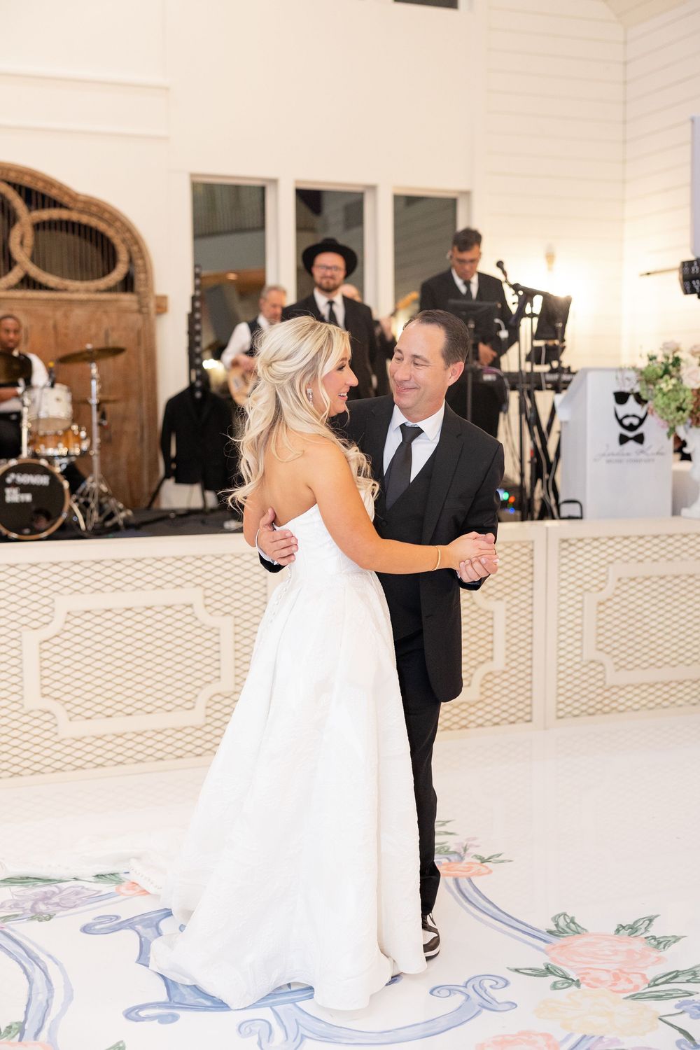 Bride shares emotional father-daughter dance on elegant floral monogram dance floor at wedding reception.