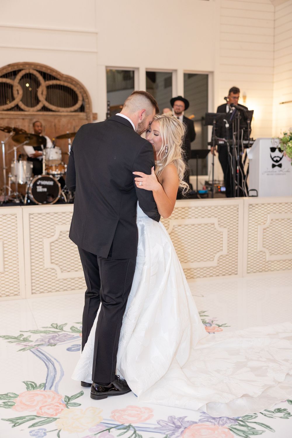 Bride and groom share intimate first dance embrace on decorated monogram dance floor with live band.