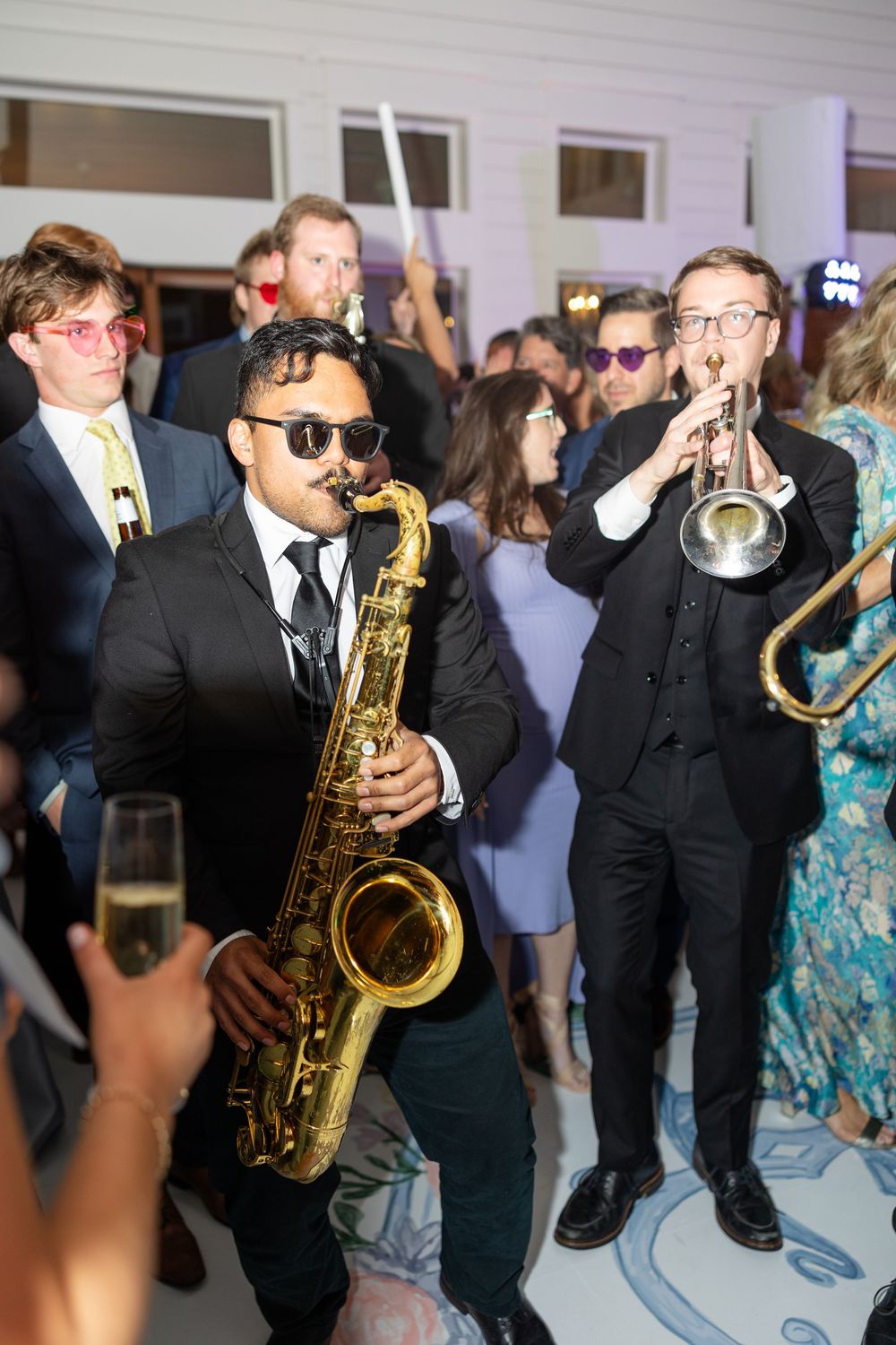 Live wedding band saxophonist and trumpet player perform energetically among celebrating reception guests.